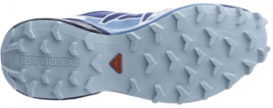 Bottom view of a trail running shoe with a rugged blue sole featuring deep treads for hiking grip, and a small red triangular logo in the middle.