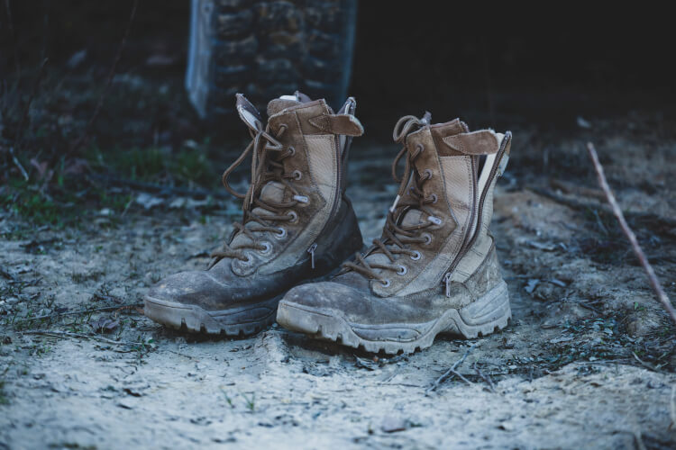 Old brown military boots on mud and grass