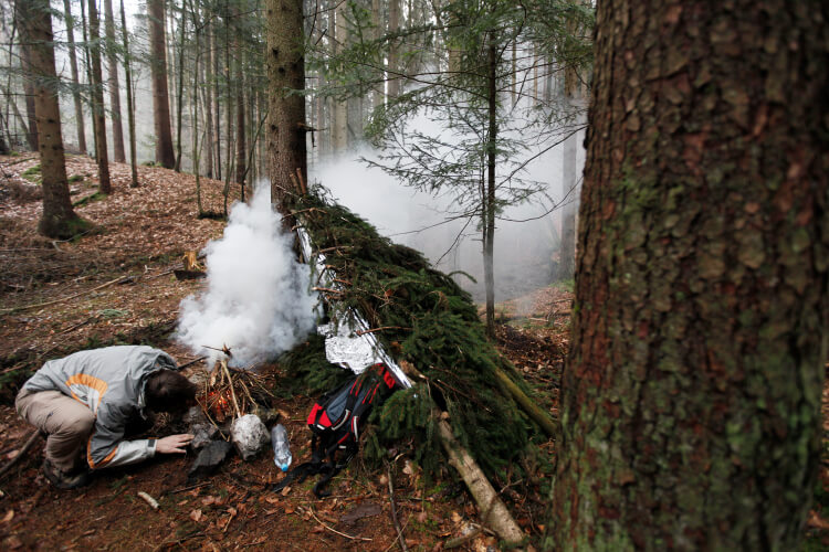 Man lighting fire next to survival shelter