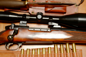 Close-up of adaptive hunting rifles with a telescopic sight and ammunition on a wooden background, exhibiting details of the polished wooden stocks and metal parts.