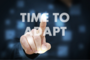 A person's finger touching the phrase "time to adapt" projected in bright, glowing letters on a digital interface, emphasizing adaptability and innovation in adaptive hiking.
