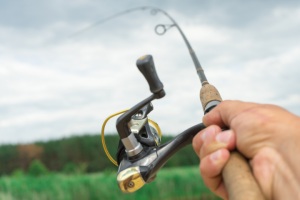 Close-up of a person holding the best fishing pole holder for wheelchair users, casting the line into a river, against a backdrop of cloudy skies and green foliage.
