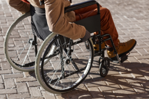 Close-up of a person in the best power wheelchair for outdoor use, focusing on the wheels and the person’s lower body, dressed in a brown jacket and yellow shoes on a cobblestone surface.