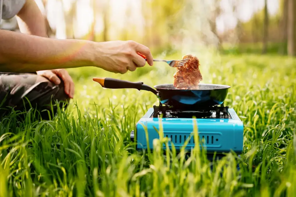 Person Cooking Meat on a Camping Stove in the Forest