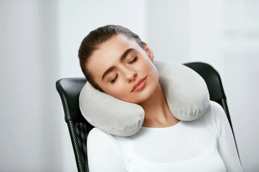 Young Woman With Pillow On Neck Sitting In Chair